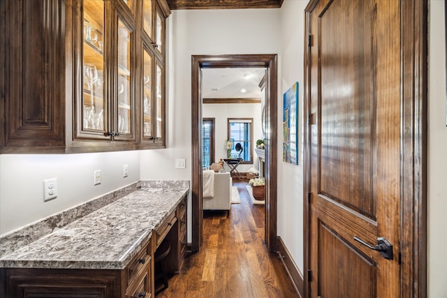 bar with built in desk, dark hardwood / wood-style floors, stone counters, and crown molding