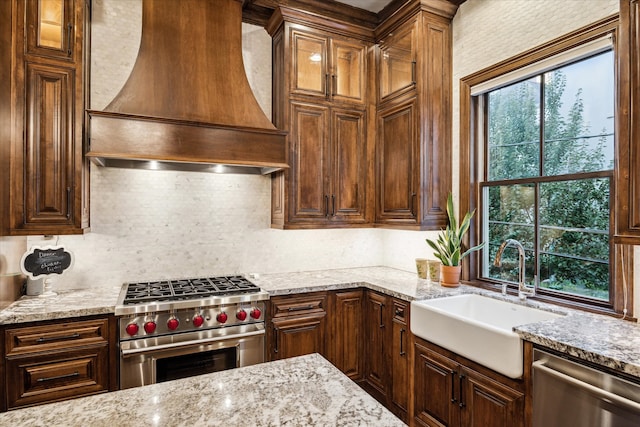 kitchen with sink, backsplash, light stone countertops, appliances with stainless steel finishes, and premium range hood