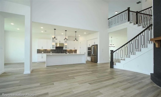 unfurnished living room featuring a chandelier, light hardwood / wood-style floors, and a towering ceiling