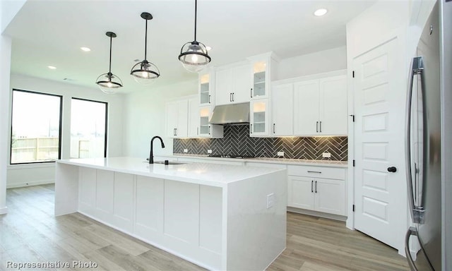 kitchen with white cabinets, decorative light fixtures, sink, a kitchen island with sink, and stainless steel refrigerator