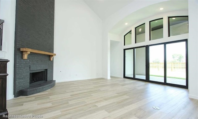 unfurnished living room with a large fireplace, high vaulted ceiling, and light hardwood / wood-style flooring