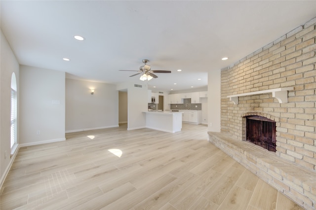 unfurnished living room featuring a brick fireplace, ceiling fan, and light wood-type flooring