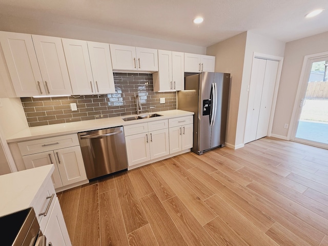 kitchen with stainless steel appliances, light hardwood / wood-style floors, white cabinetry, sink, and tasteful backsplash