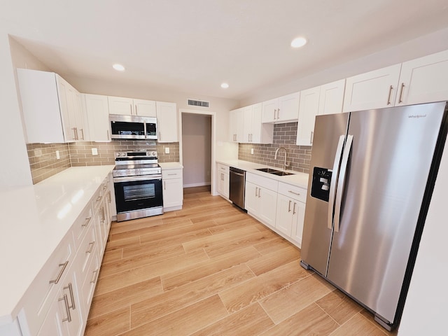 kitchen featuring stainless steel appliances, sink, backsplash, white cabinets, and light wood-type flooring