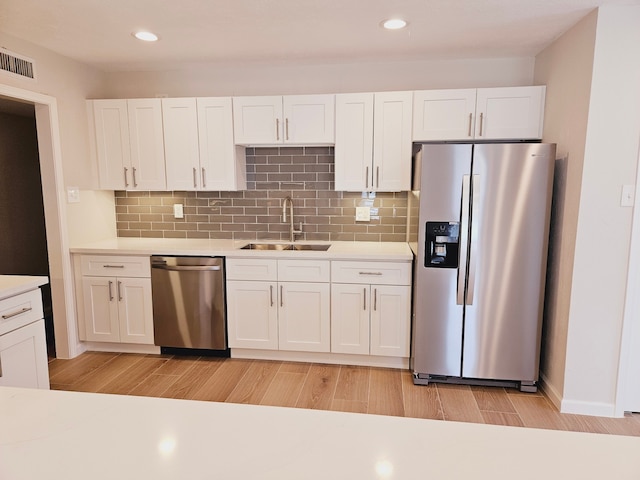 kitchen with decorative backsplash, sink, white cabinetry, light wood-type flooring, and appliances with stainless steel finishes