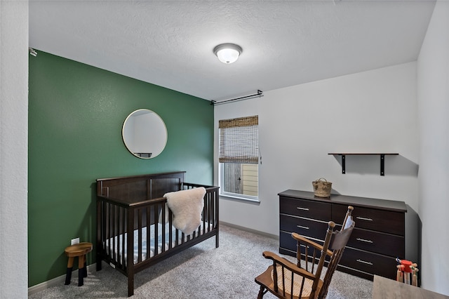 carpeted bedroom featuring a textured ceiling and a nursery area