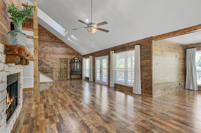 unfurnished living room featuring a stone fireplace, wood walls, plenty of natural light, and a skylight