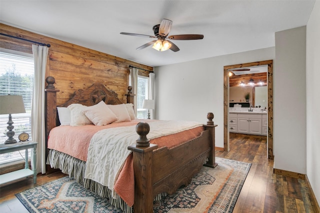 bedroom featuring ceiling fan, dark hardwood / wood-style flooring, wooden walls, and ensuite bath