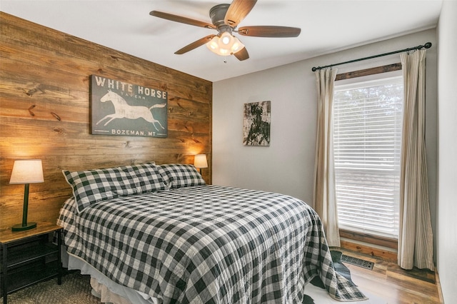 bedroom featuring multiple windows, wood-type flooring, ceiling fan, and wooden walls