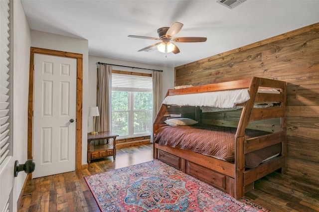 bedroom with ceiling fan, dark wood-type flooring, and wood walls