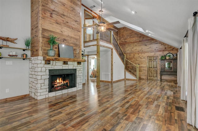 unfurnished living room featuring high vaulted ceiling, a stone fireplace, ceiling fan, and wooden walls