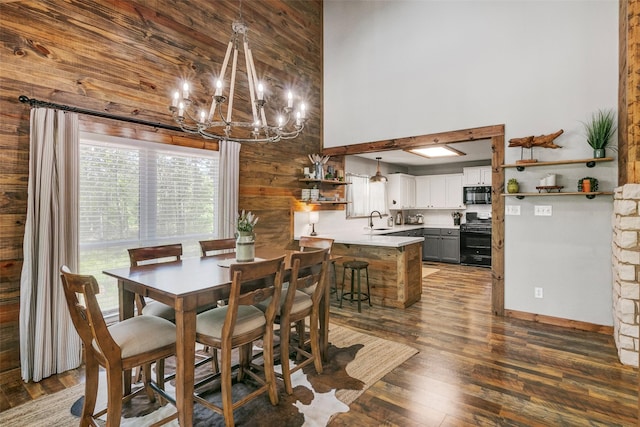 dining area featuring a towering ceiling, dark hardwood / wood-style flooring, sink, a chandelier, and wood walls