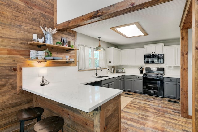 kitchen with a kitchen bar, sink, black appliances, decorative light fixtures, and white cabinetry