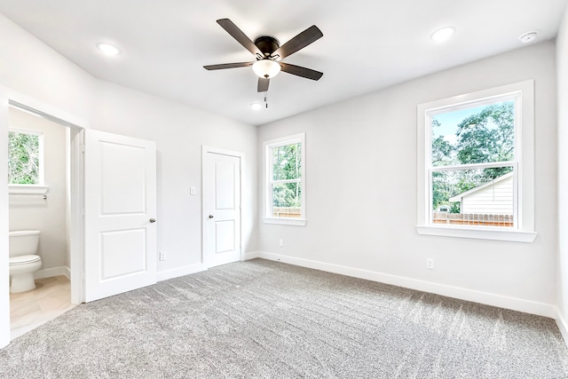 unfurnished bedroom featuring ensuite bath, ceiling fan, multiple windows, and carpet