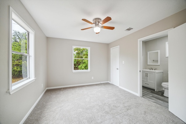 unfurnished bedroom with ensuite bath, carpet flooring, and ceiling fan