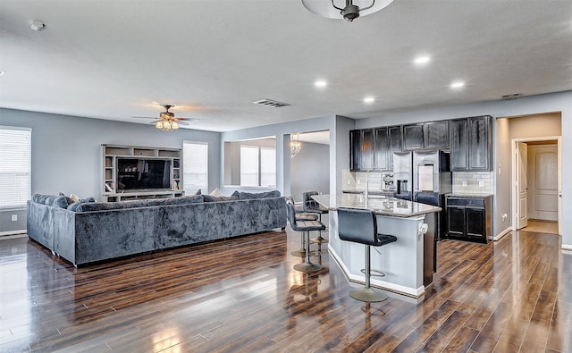 kitchen with an island with sink, a kitchen breakfast bar, light stone counters, and dark hardwood / wood-style flooring