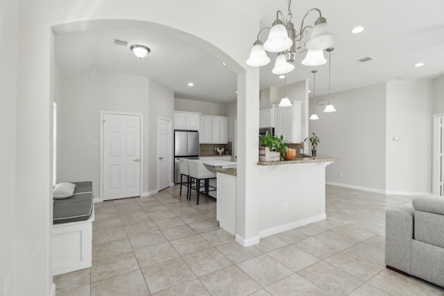 kitchen with kitchen peninsula, light stone countertops, light tile patterned floors, white cabinetry, and stainless steel refrigerator