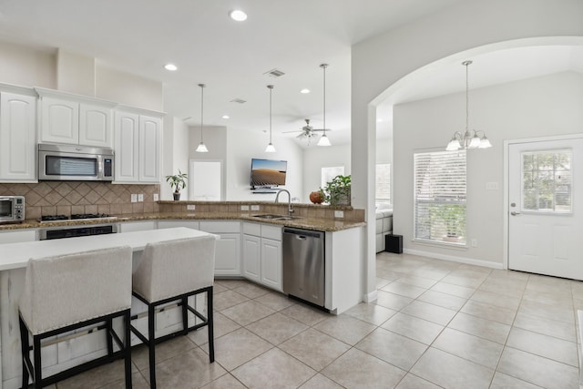 kitchen with kitchen peninsula, white cabinets, pendant lighting, appliances with stainless steel finishes, and ceiling fan with notable chandelier