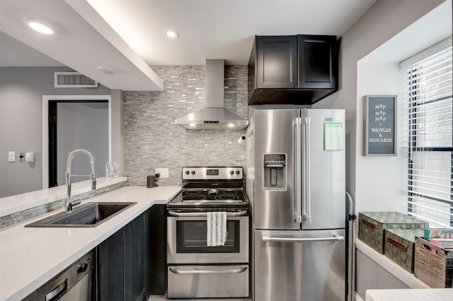 kitchen with decorative backsplash, wall chimney range hood, sink, appliances with stainless steel finishes, and light stone counters