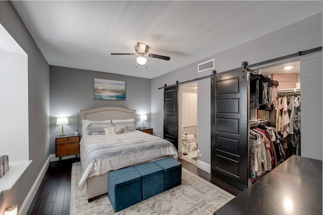 bedroom featuring dark hardwood / wood-style floors, a closet, a walk in closet, a barn door, and ceiling fan