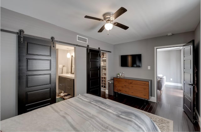 bedroom featuring ceiling fan, dark hardwood / wood-style flooring, a barn door, and ensuite bathroom