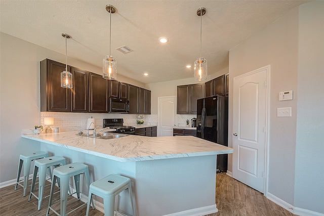 kitchen featuring black appliances, tasteful backsplash, wood-type flooring, hanging light fixtures, and kitchen peninsula