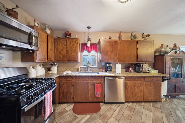 kitchen with a textured ceiling, stainless steel appliances, sink, pendant lighting, and light hardwood / wood-style floors