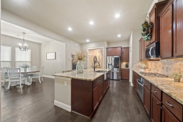 kitchen featuring appliances with stainless steel finishes, decorative light fixtures, a center island with sink, and dark hardwood / wood-style flooring