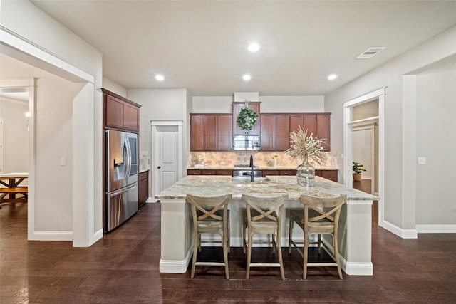 kitchen featuring decorative backsplash, stainless steel appliances, light stone countertops, and a center island with sink