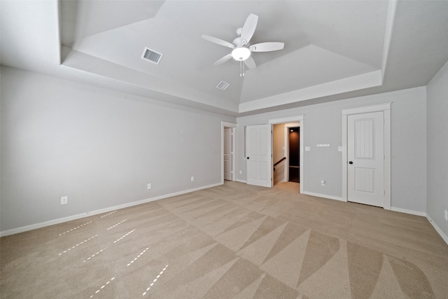 unfurnished bedroom with ceiling fan, a raised ceiling, and light colored carpet