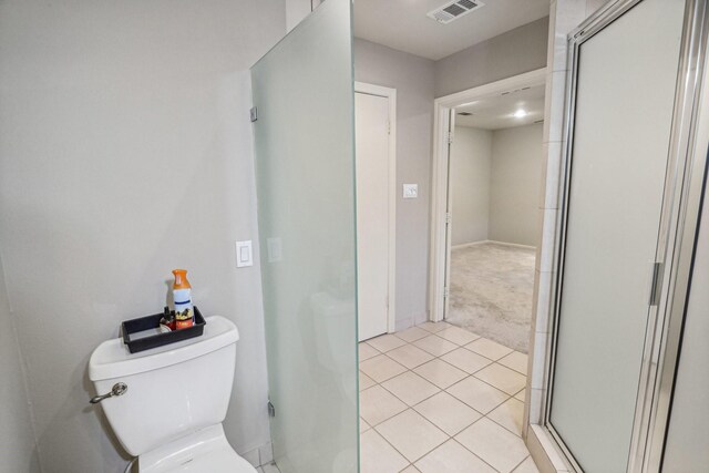 bathroom featuring a shower with door, toilet, and tile patterned flooring