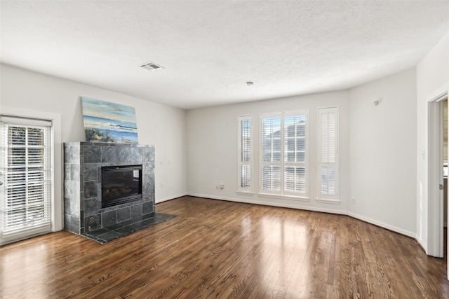 unfurnished living room with dark hardwood / wood-style floors, a tiled fireplace, and a textured ceiling