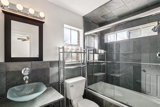 full bathroom featuring shower / bath combination with glass door, toilet, ceiling fan, tile walls, and vanity