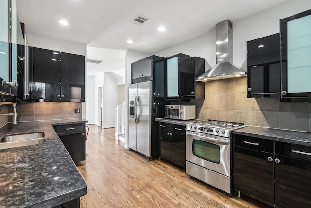 kitchen with wall chimney range hood, sink, backsplash, light hardwood / wood-style floors, and stainless steel appliances