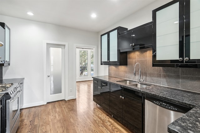 kitchen featuring decorative backsplash, appliances with stainless steel finishes, light wood-type flooring, dark stone countertops, and sink