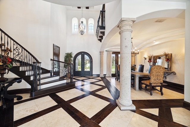 entryway featuring ornate columns, french doors, a high ceiling, and a notable chandelier