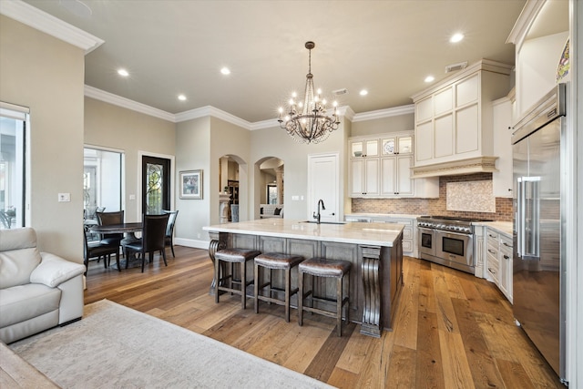 kitchen featuring hanging light fixtures, premium appliances, crown molding, an island with sink, and light wood-type flooring