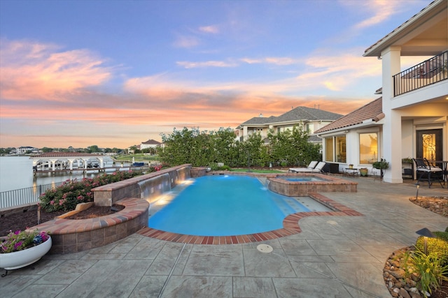 pool at dusk featuring an in ground hot tub, a patio, a water view, and pool water feature