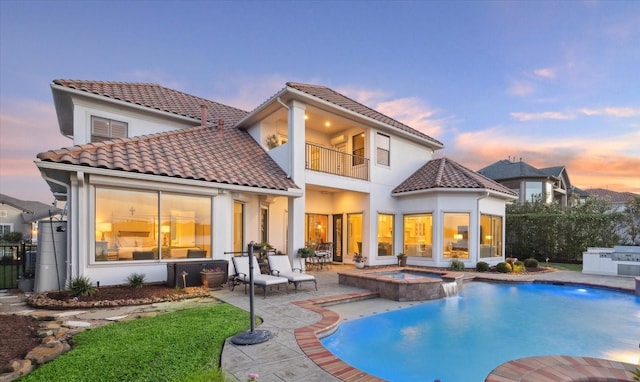 back house at dusk with a swimming pool with hot tub, a balcony, and a patio