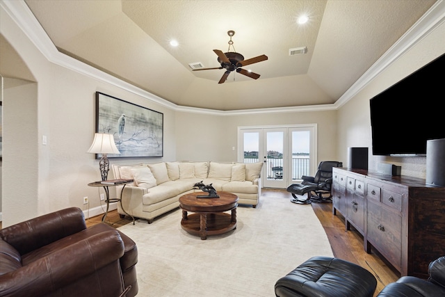 living room featuring ceiling fan, french doors, light hardwood / wood-style floors, a tray ceiling, and ornamental molding