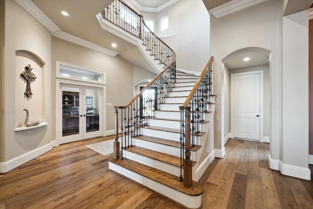 stairs featuring hardwood / wood-style floors, a towering ceiling, french doors, and ornamental molding