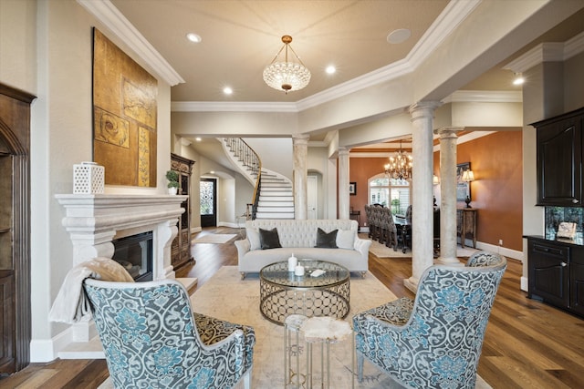 living room with decorative columns, crown molding, wood-type flooring, and an inviting chandelier