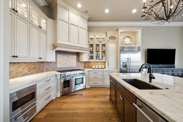 kitchen with high end appliances, sink, light wood-type flooring, ornamental molding, and a chandelier