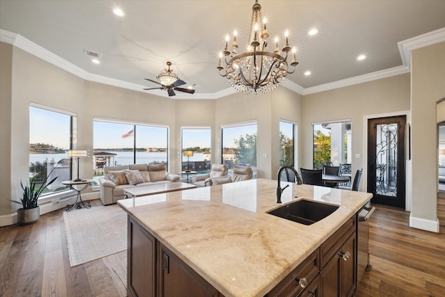 kitchen with sink, dark hardwood / wood-style floors, crown molding, an island with sink, and a water view