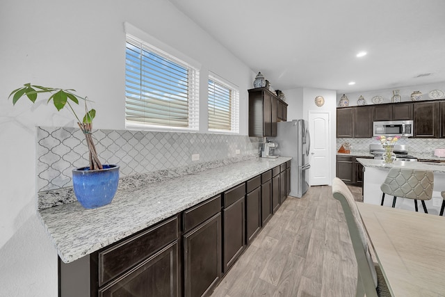 kitchen with decorative backsplash, a barn door, light hardwood / wood-style floors, dark brown cabinetry, and stainless steel appliances