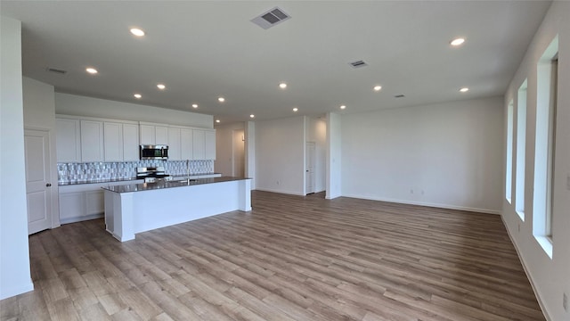 kitchen featuring white cabinetry, stainless steel appliances, backsplash, a center island with sink, and light wood-type flooring