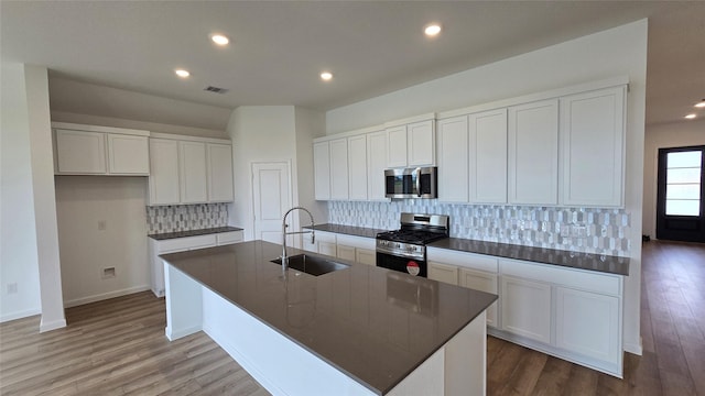 kitchen featuring hardwood / wood-style floors, a kitchen island with sink, sink, appliances with stainless steel finishes, and white cabinetry