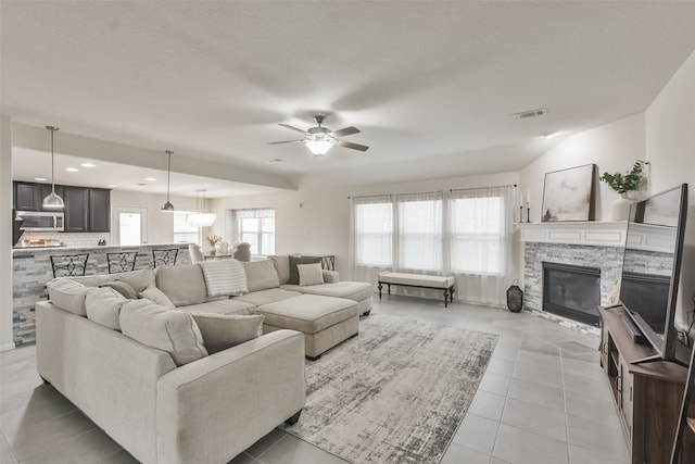 living room with a stone fireplace, light tile patterned floors, and ceiling fan