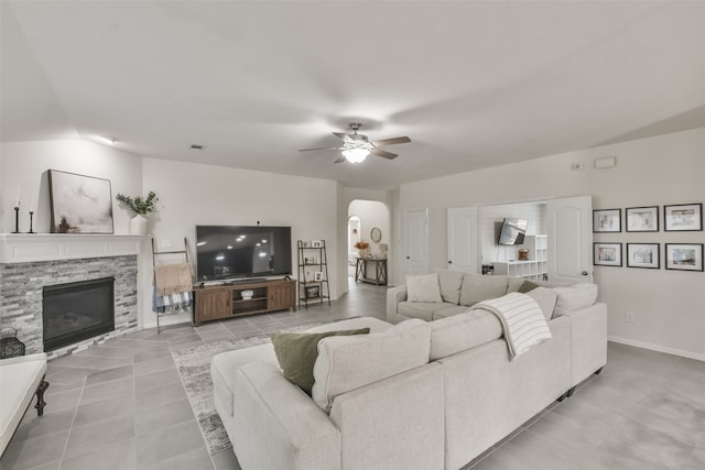 living room with a stone fireplace, light tile patterned floors, and ceiling fan