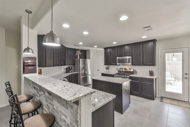 kitchen with kitchen peninsula, stainless steel appliances, a breakfast bar, pendant lighting, and tasteful backsplash